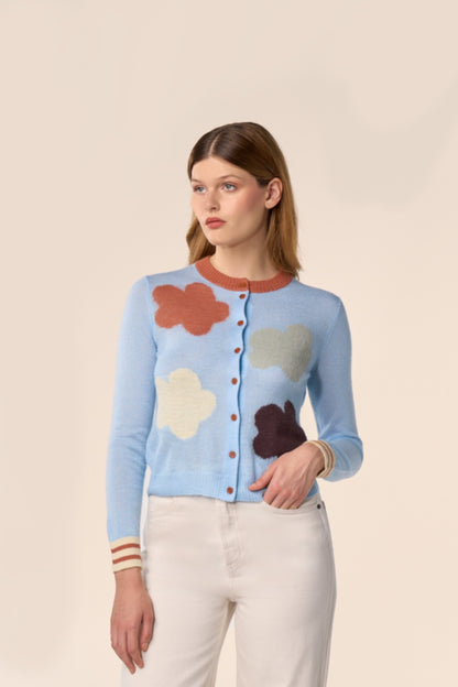 Cardigan bleu ciel en maille, manches longues, motifs nuages multicolores et poignets rayés, porté avec un pantalon écru — Pote aux Roses Paris
