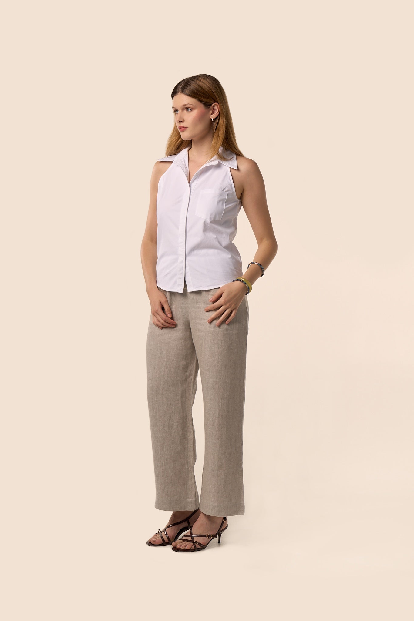 Chemise blanche sans manches à col classique, coupe ajustée et poche plaquée, portée avec un pantalon beige en lin mélangé — Pote aux Roses Paris